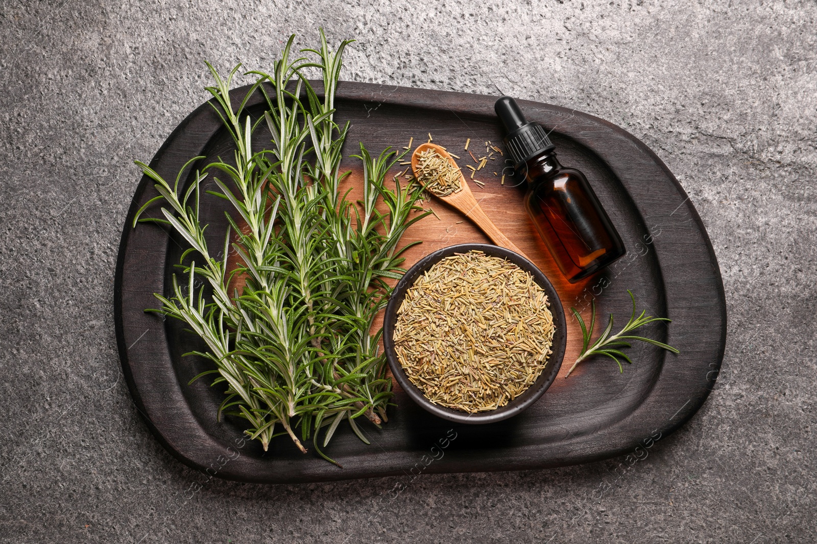 Photo of Bottle of essential oil, fresh and dry rosemary on grey table, top view