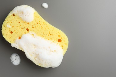 Photo of Yellow sponge with foam on grey background, top view. Space for text