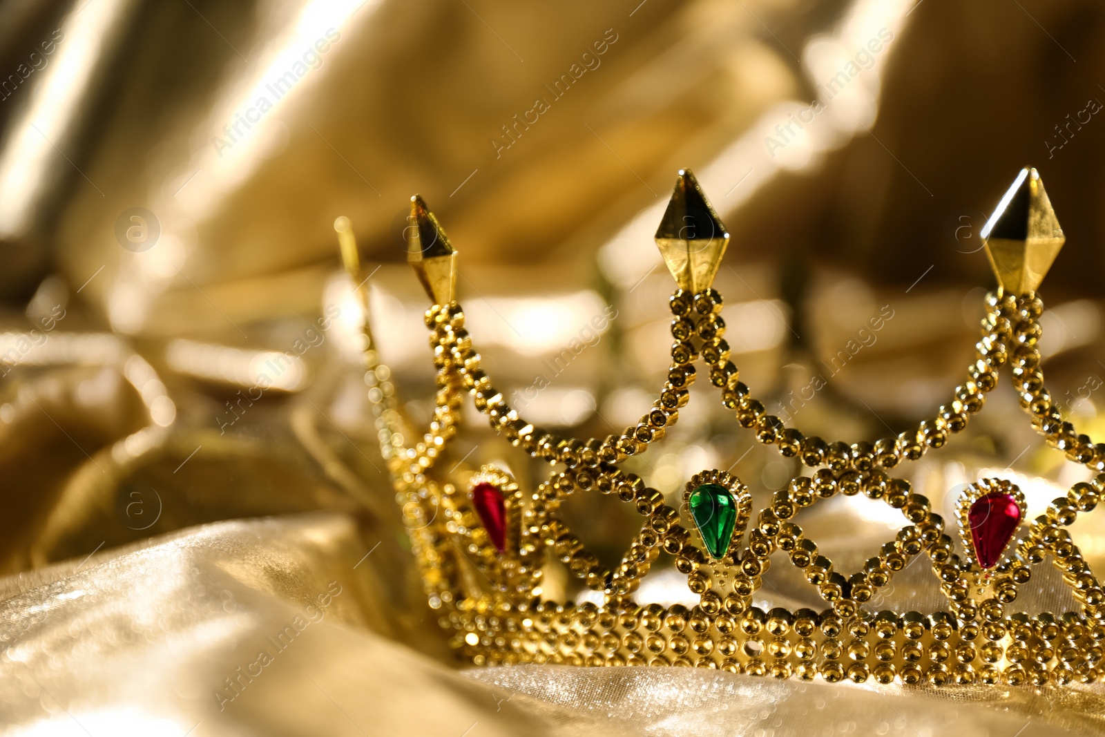 Photo of Beautiful ancient crown on golden fabric, closeup. Fantasy item