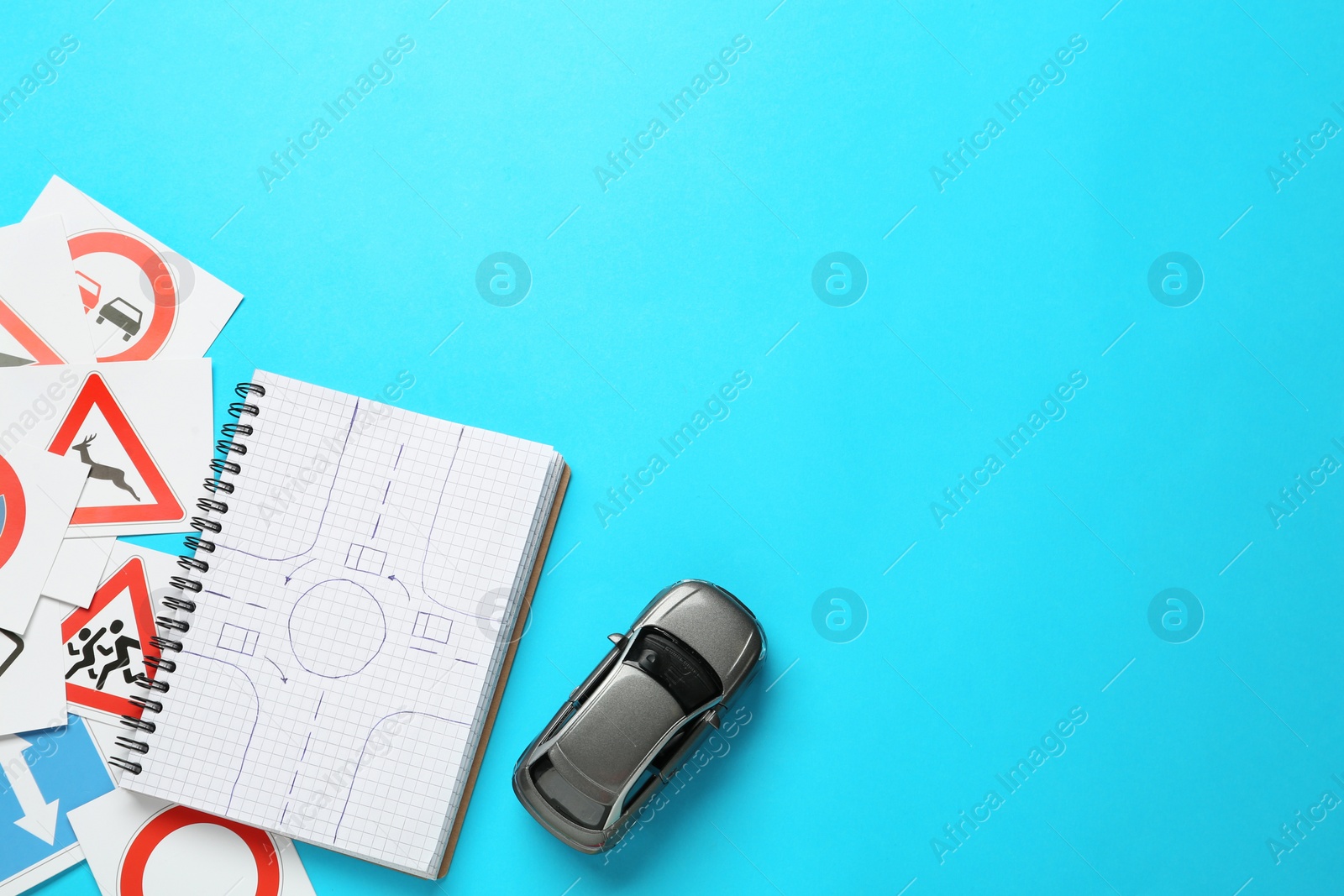 Photo of Many different road sign cards, notebook and toy car on light blue background, flat lay with space for text. Driving school