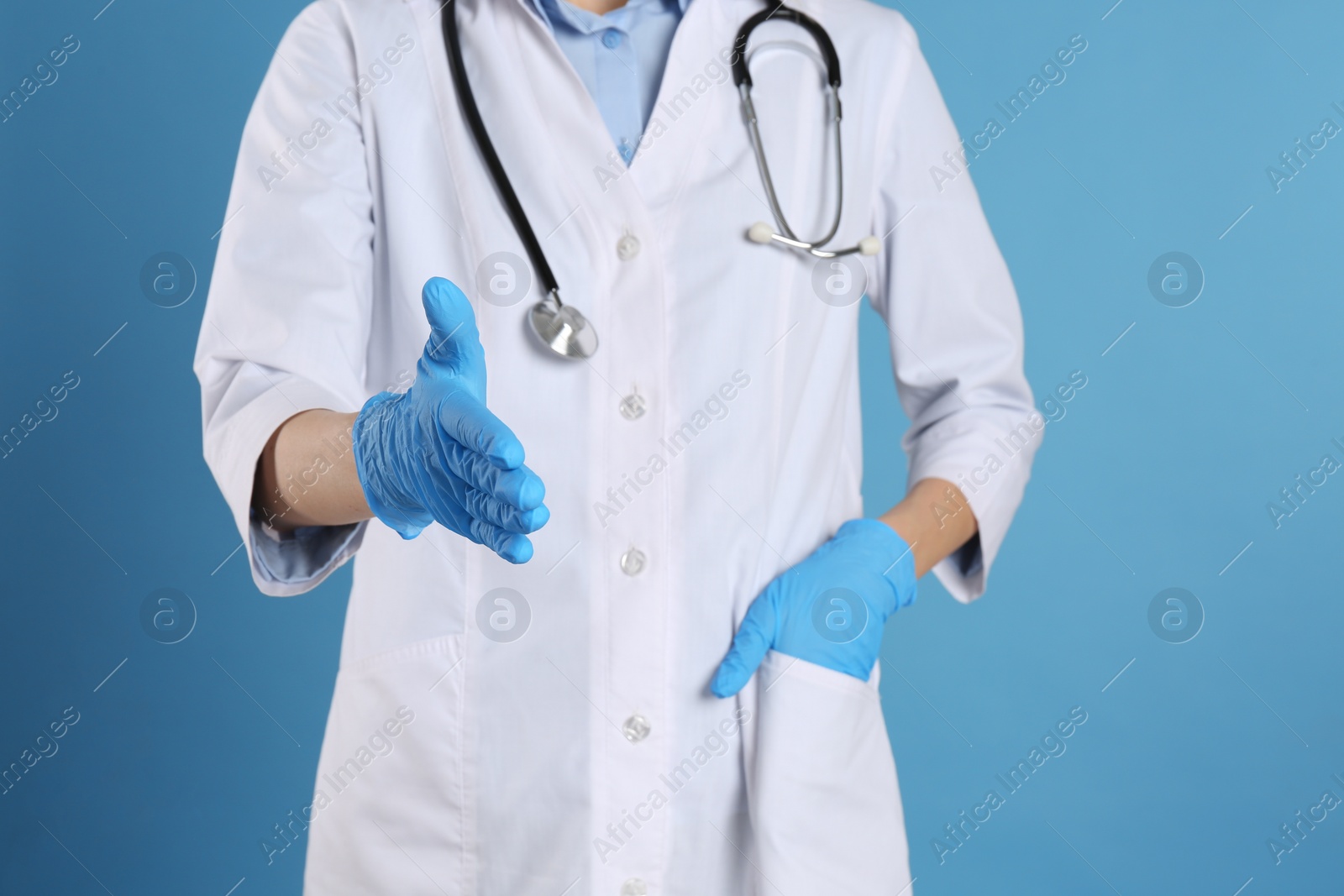 Photo of Female doctor in gloves offering handshake on light blue background, closeup