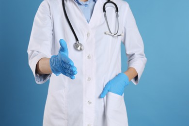 Female doctor in gloves offering handshake on light blue background, closeup