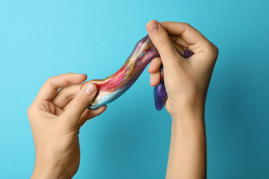 Photo of Woman playing with colorful slime on light blue background, closeup. Antistress toy
