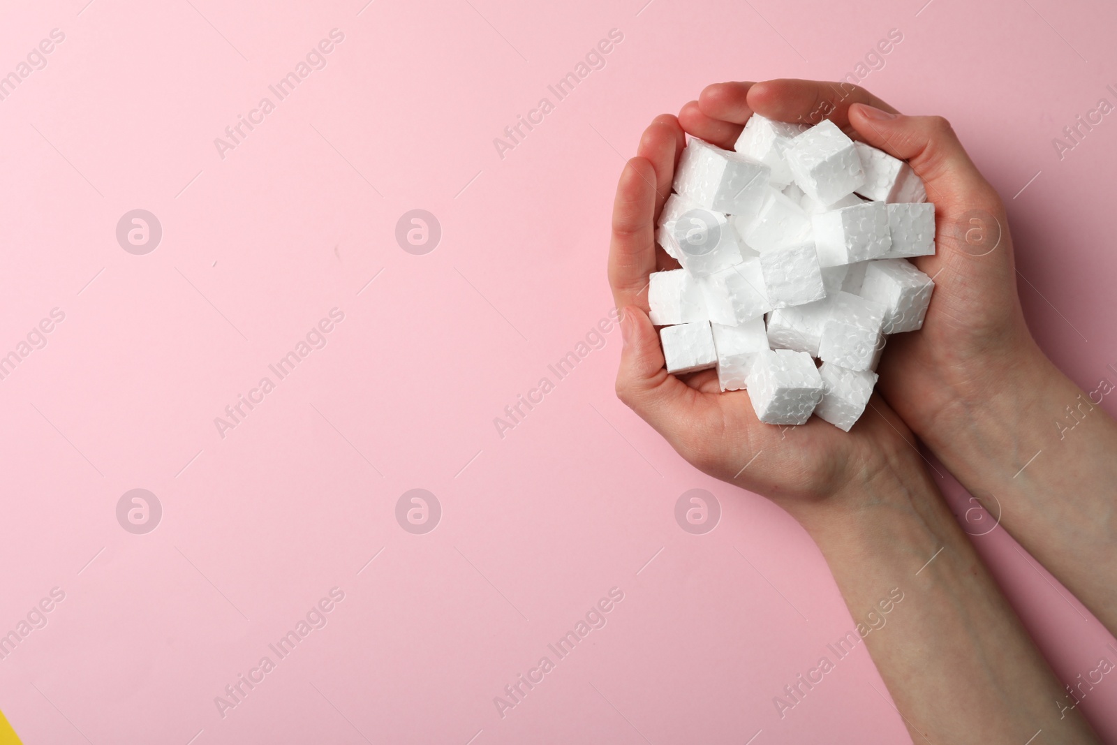 Photo of Woman with handful of styrofoam cubes on pink background, top view. Space for text