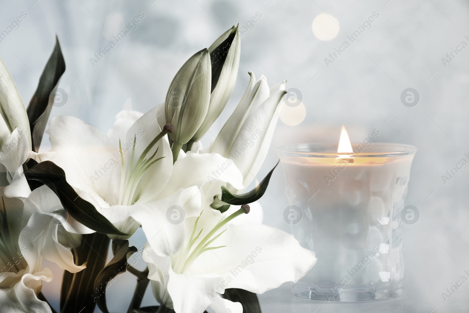 Image of Funeral. Beautiful lilies and burning candle on light blurred background, bokeh effect.