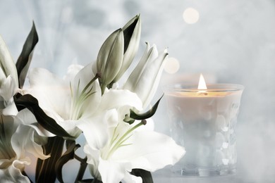 Image of Funeral. Beautiful lilies and burning candle on light blurred background, bokeh effect.