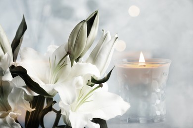 Funeral. Beautiful lilies and burning candle on light blurred background, bokeh effect.