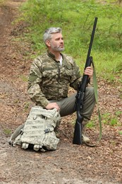 Man with hunting rifle and backpack wearing camouflage in forest