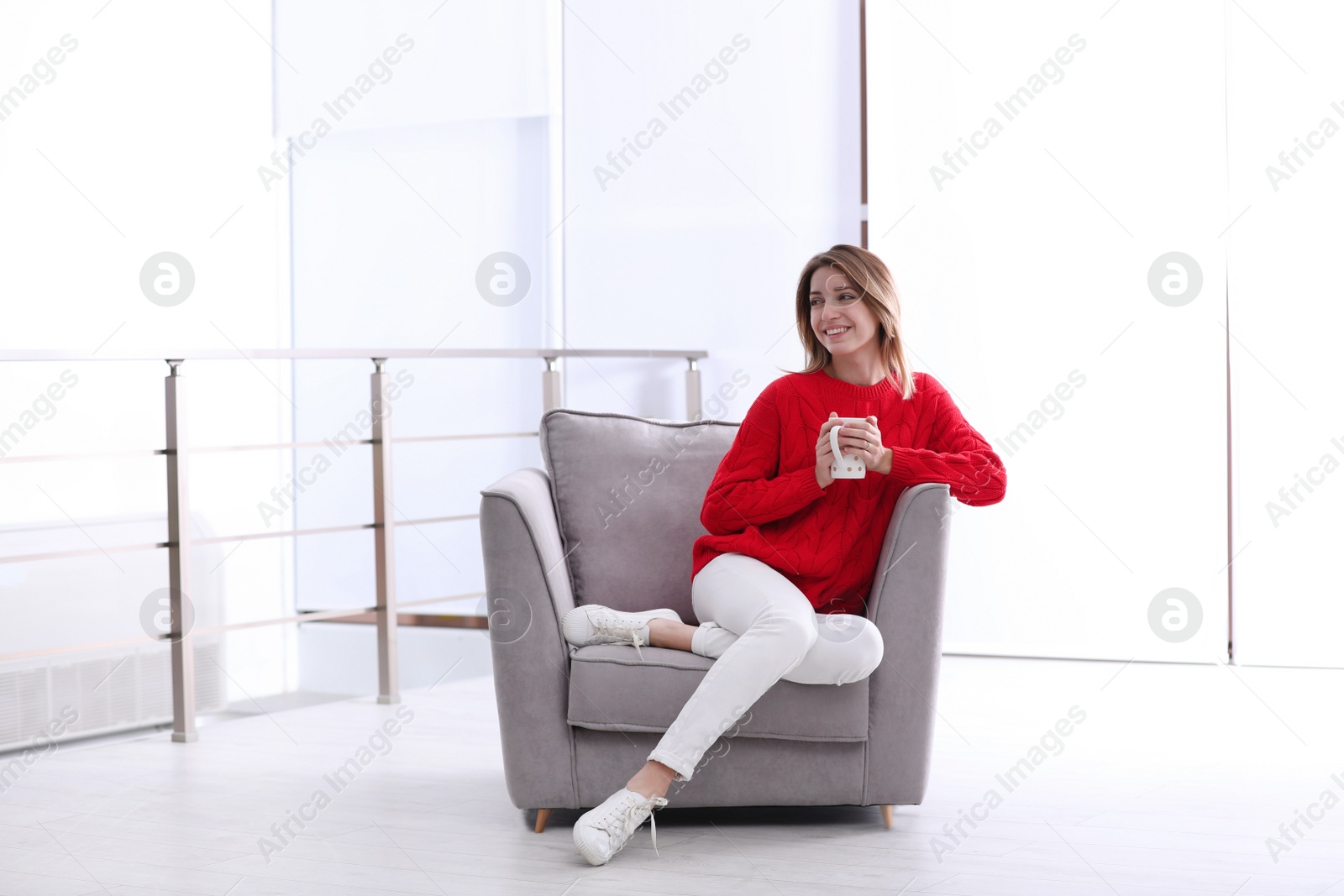Photo of Attractive young woman with cup of tea in armchair indoors