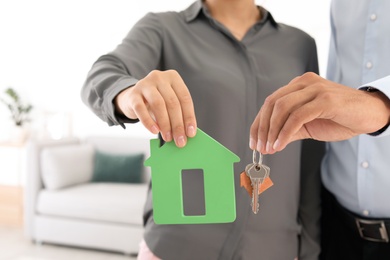 Young couple holding keys and house model, closeup. Real estate agent services