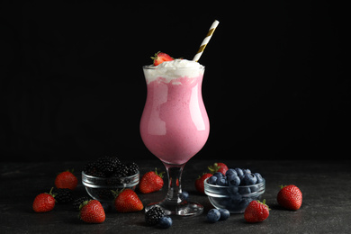 Photo of Tasty milk shake with whipped cream and fresh berries on black slate table