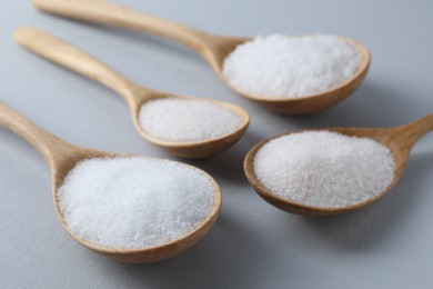 Photo of Organic white salt in spoons on light grey background, closeup