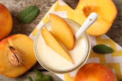 Photo of Tasty peach yogurt with pieces of fruit and spoon in glass jar on wooden table, flat lay