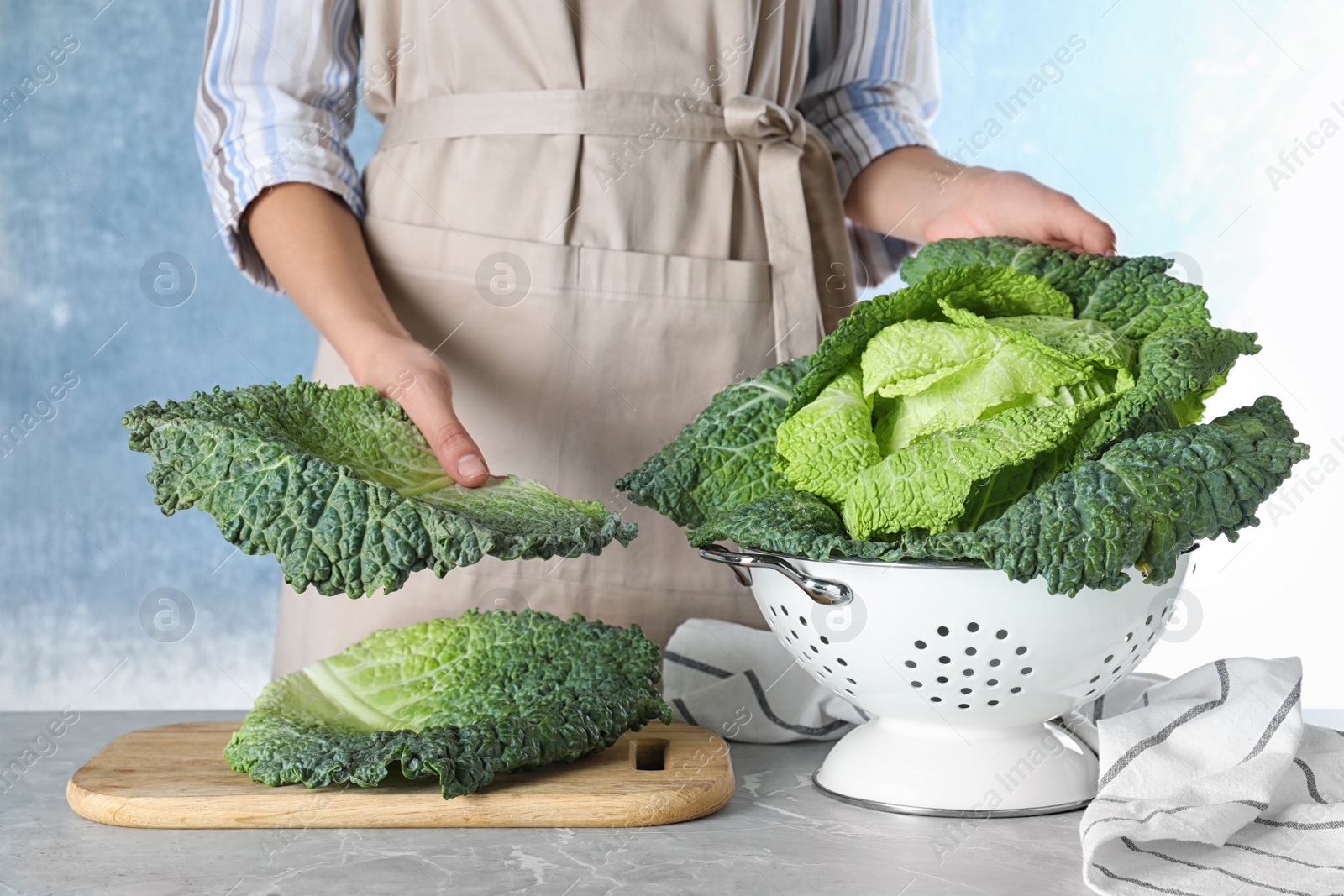 Photo of Woman with fresh green savoy cabbage at table against light blue background, closeup
