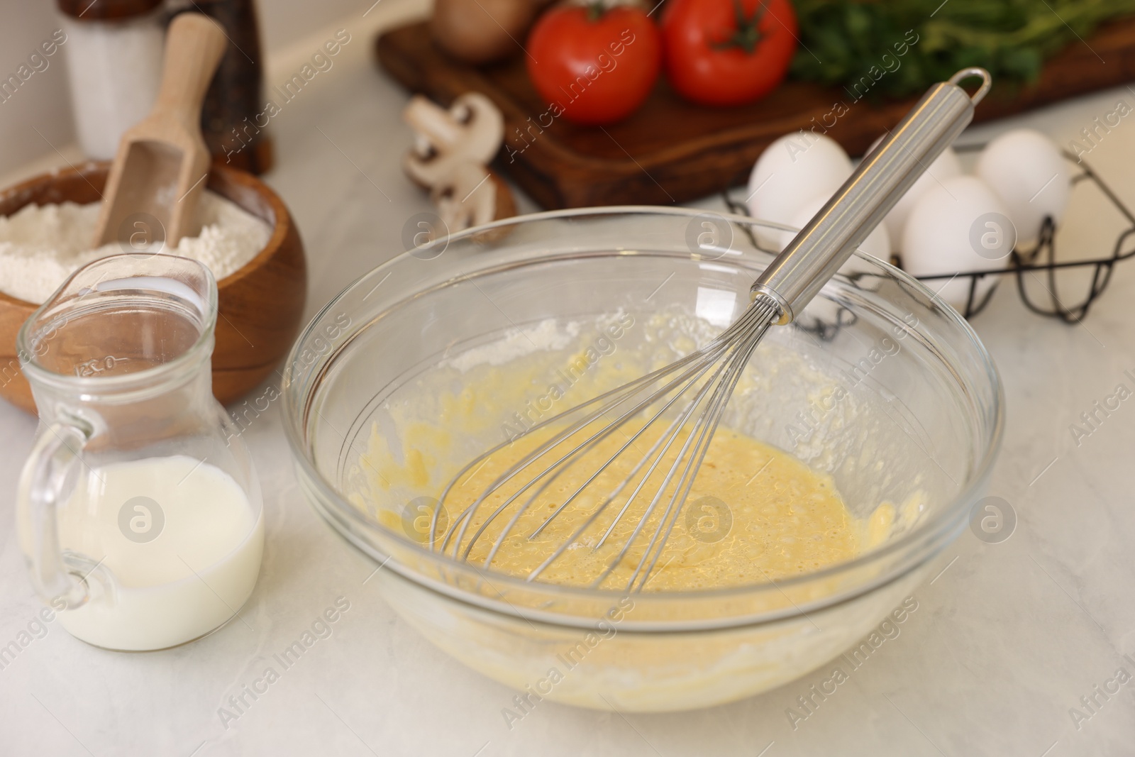 Photo of Metal whisk, cream in bowl and different products on light table