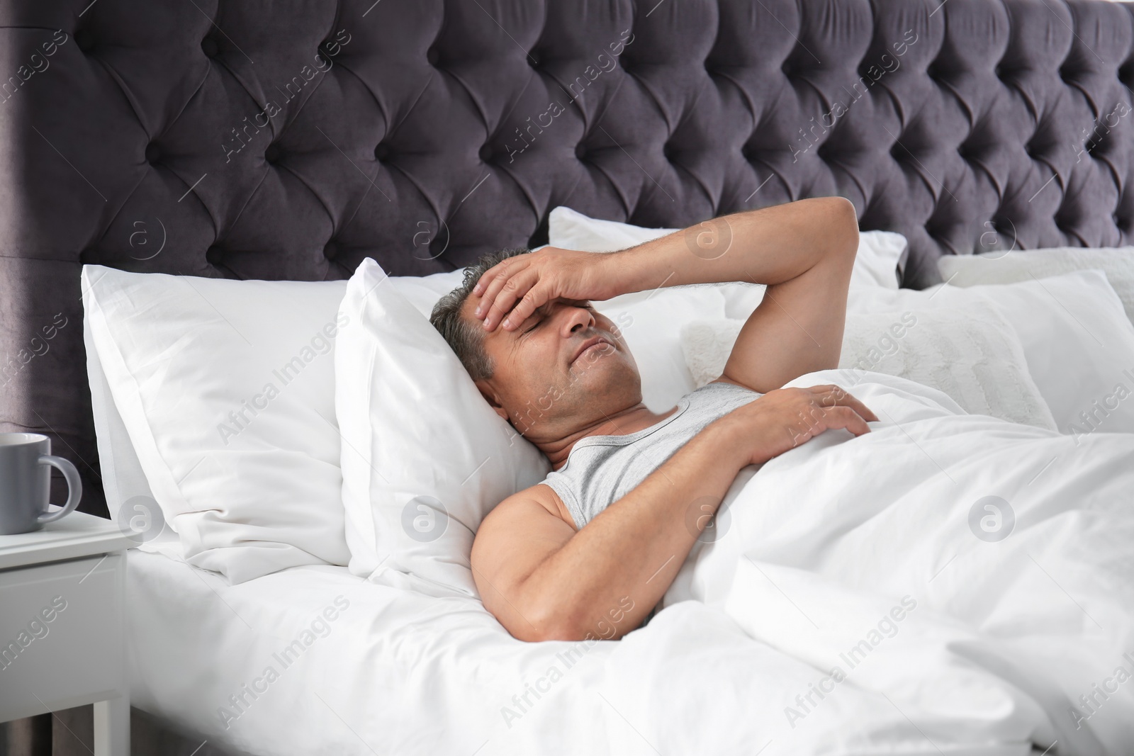 Photo of Man suffering from headache after sleep in bed. Uncomfortable pillow