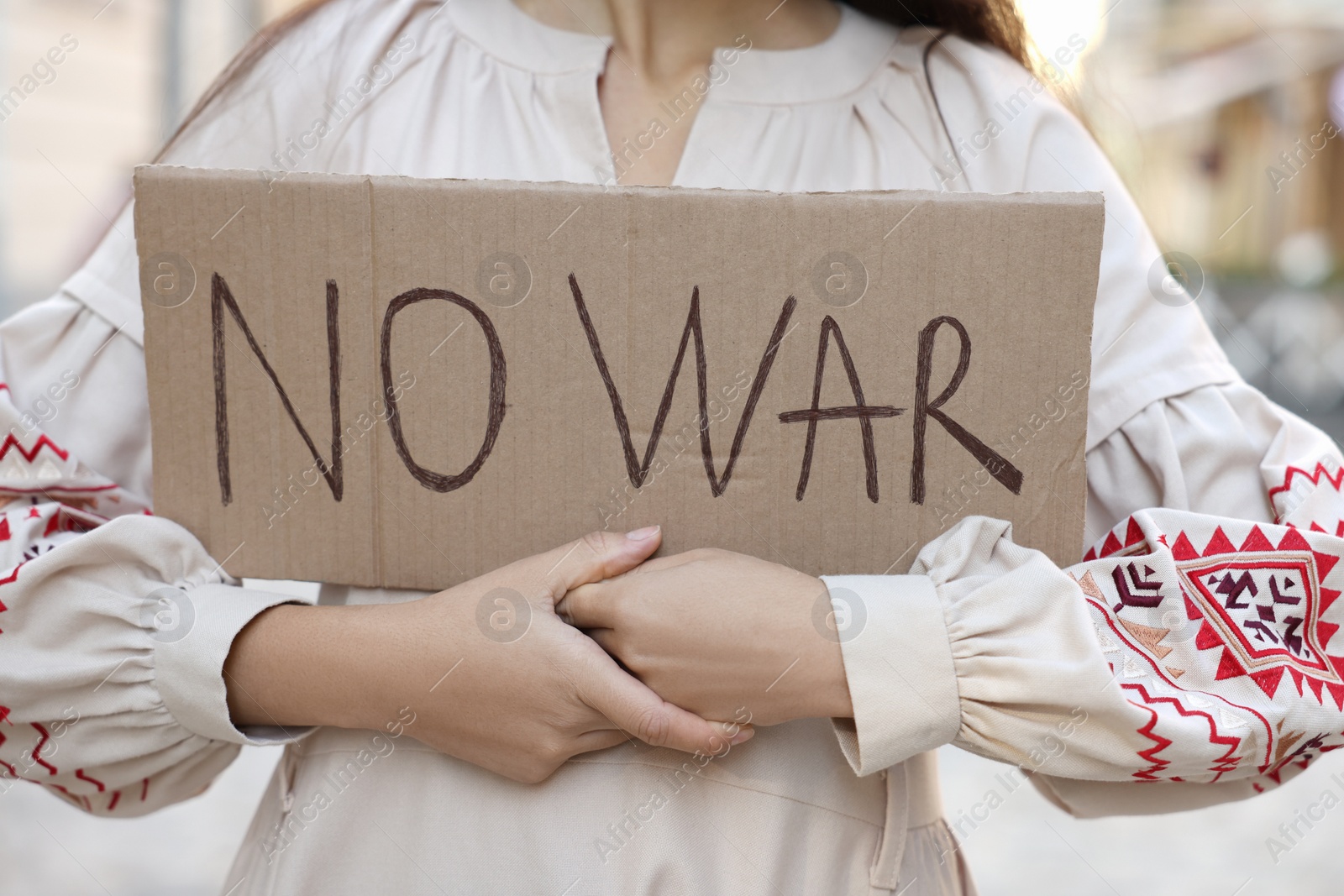 Photo of Woman in embroidered dress holding poster No War outdoors, closeup