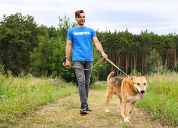 Photo of Male volunteer with homeless dog at animal shelter outdoors