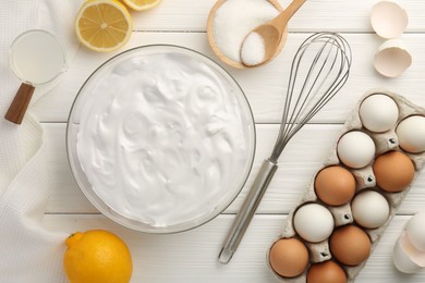 Bowl with whipped cream, whisk and ingredients on white wooden table, flat lay