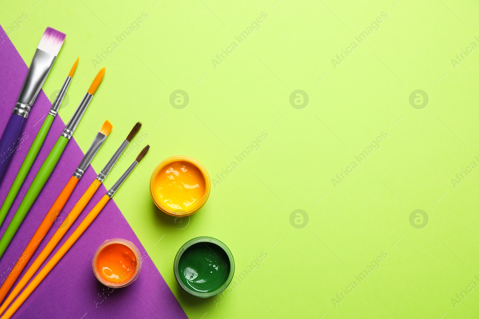 Photo of Brushes and bright paints on color background, flat lay. Space for text