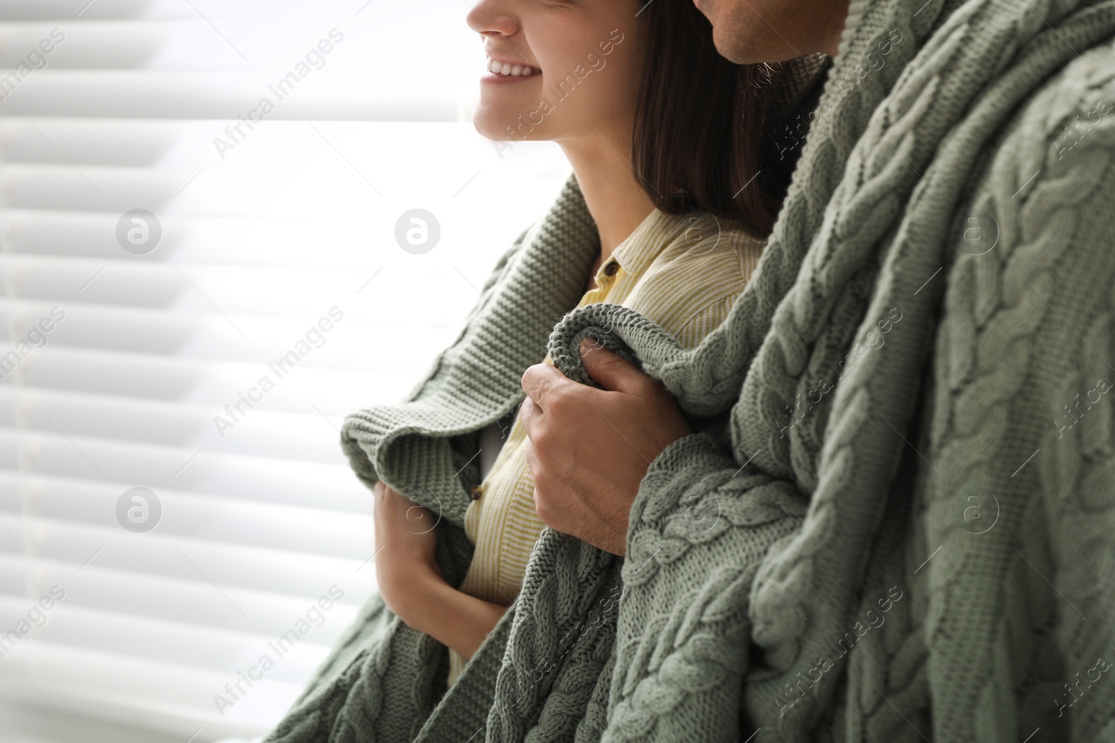 Photo of Happy couple covered with warm green plaid near window indoors, closeup