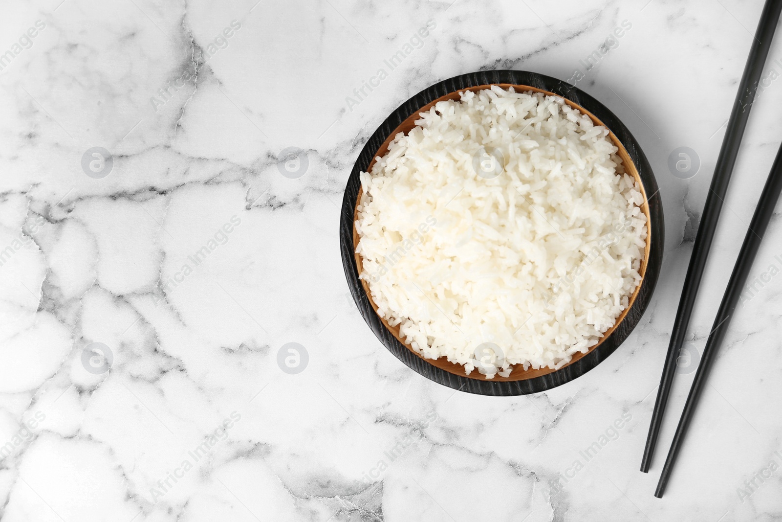 Photo of Bowl of boiled rice and chopsticks on marble background, top view with space for text