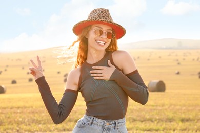 Photo of Beautiful happy hippie woman in hat showing peace sign in field