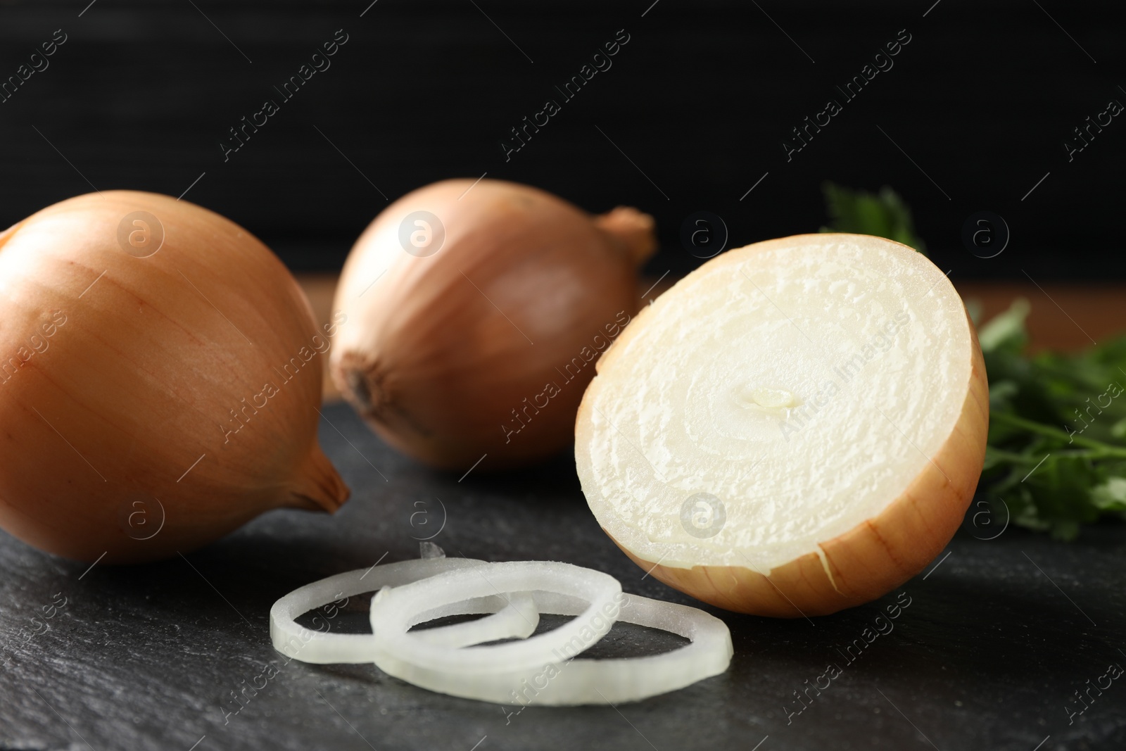 Photo of Whole and cut onions on black textured table, closeup