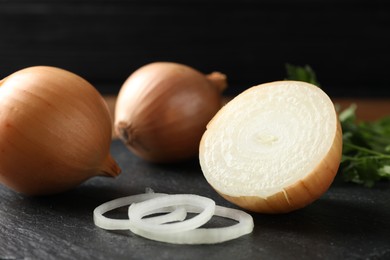 Whole and cut onions on black textured table, closeup