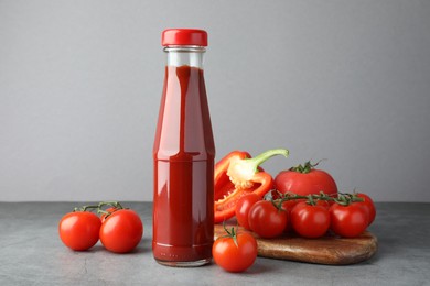 Bottle of tasty ketchup, tomatoes and pepper on grey table