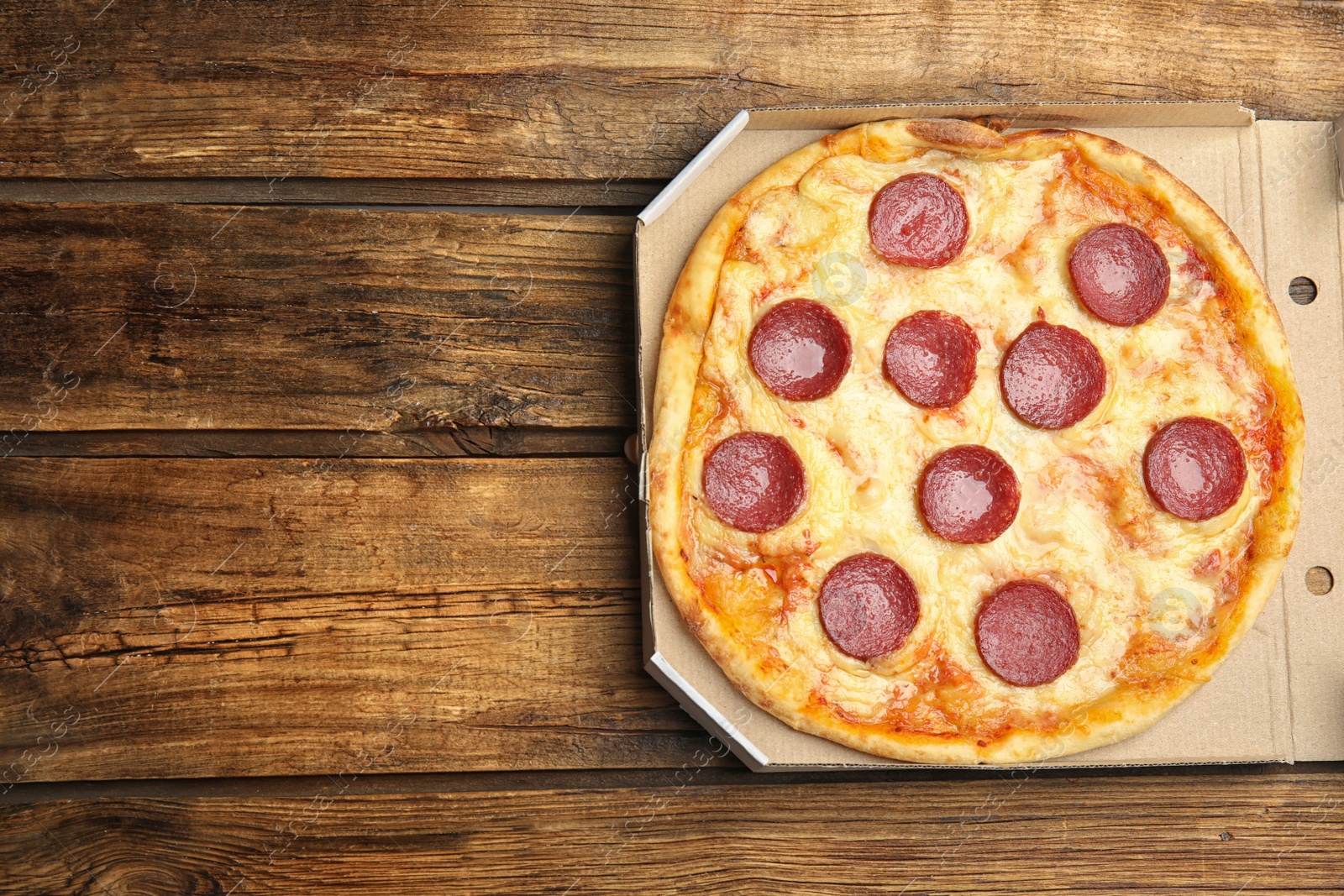 Photo of Tasty pepperoni pizza in cardboard box on wooden table, top view. Space for text