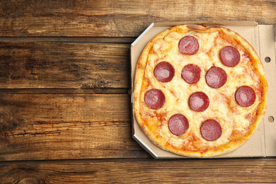 Photo of Tasty pepperoni pizza in cardboard box on wooden table, top view. Space for text
