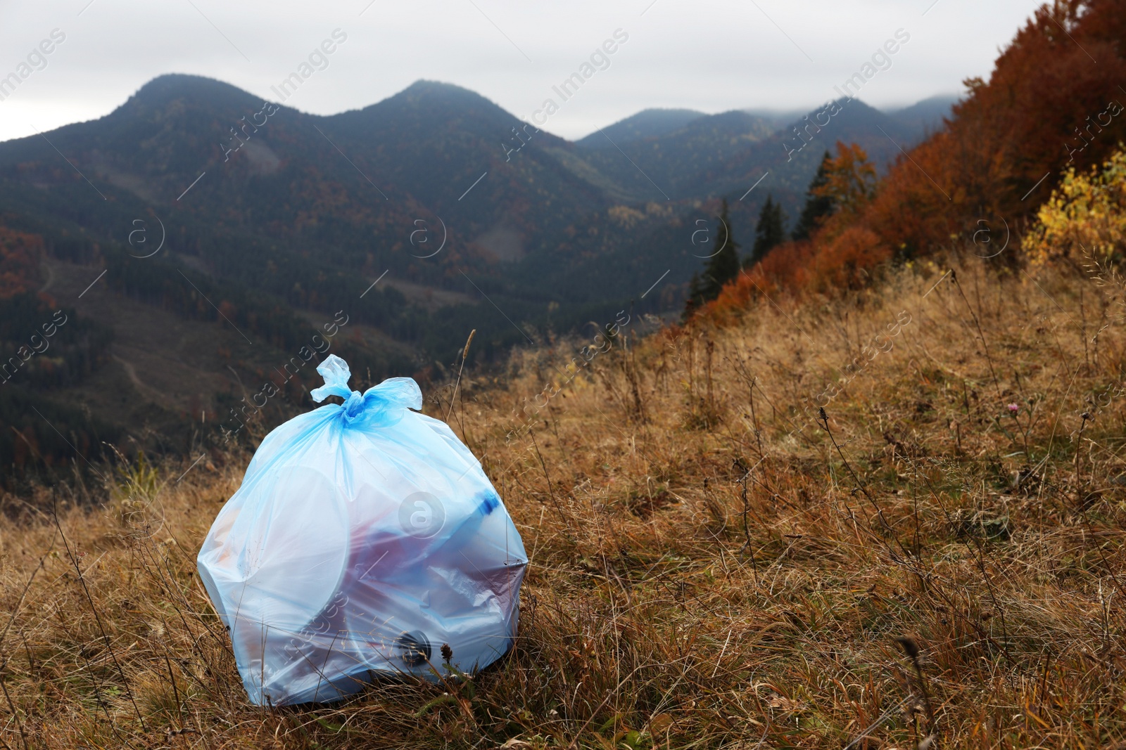 Photo of Trash bag full of garbage on ground against mountain landscape. Space for text