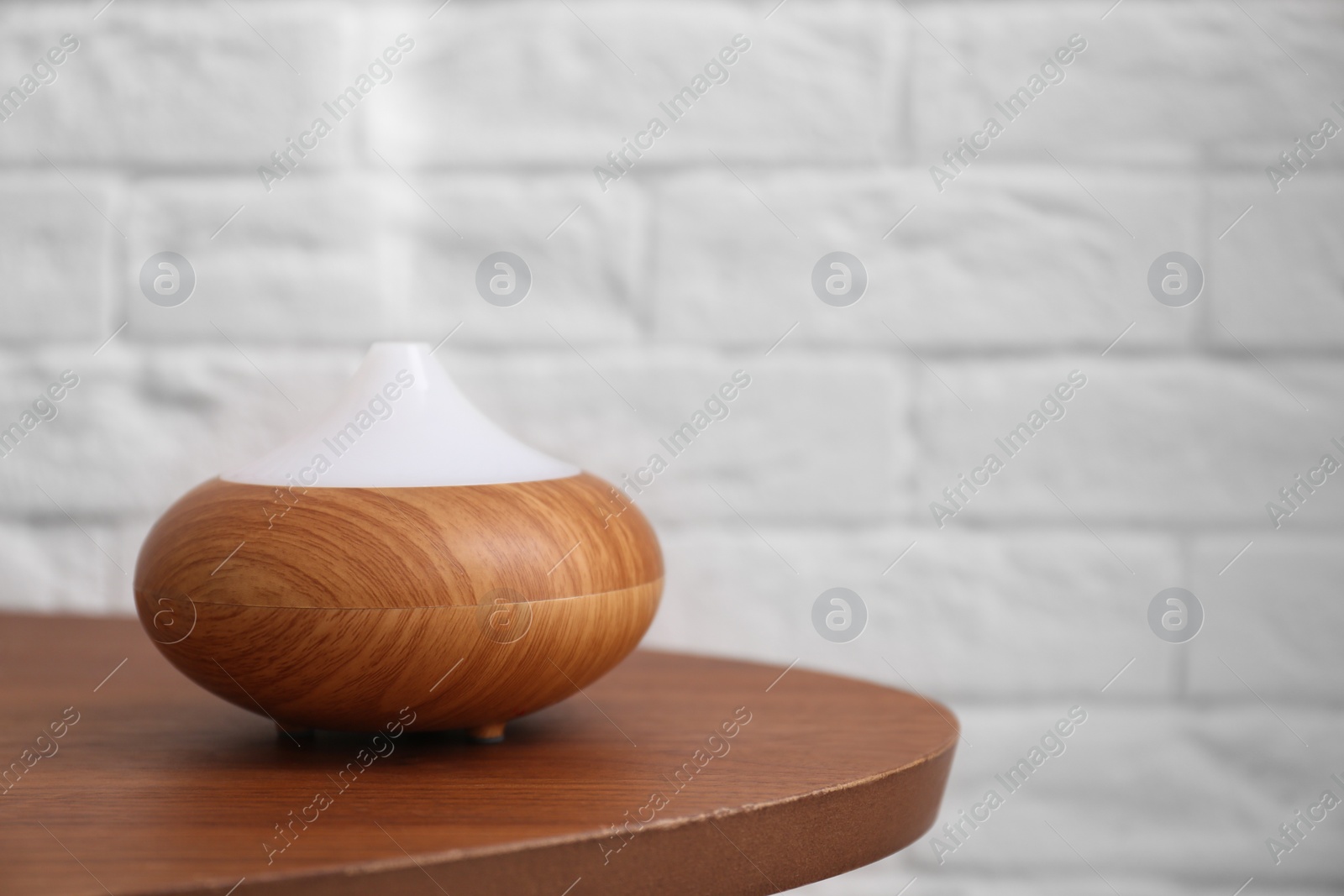 Photo of Essential oils diffuser on wooden table   against brick wall. Space for text