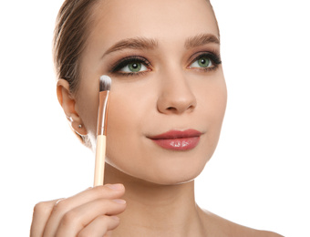 Beautiful woman applying makeup with brush on white background