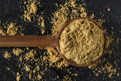 Photo of Wooden spoon of aromatic mustard powder on black table, top view