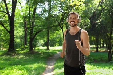 Photo of Handsome man with headphones running in park, space for text. Morning exercise