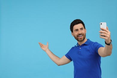 Photo of Smiling man taking selfie with smartphone on light blue background, space for text