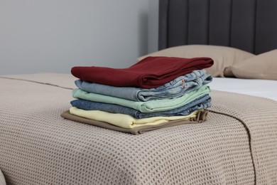 Photo of Stack of different folded clothes on bed at home