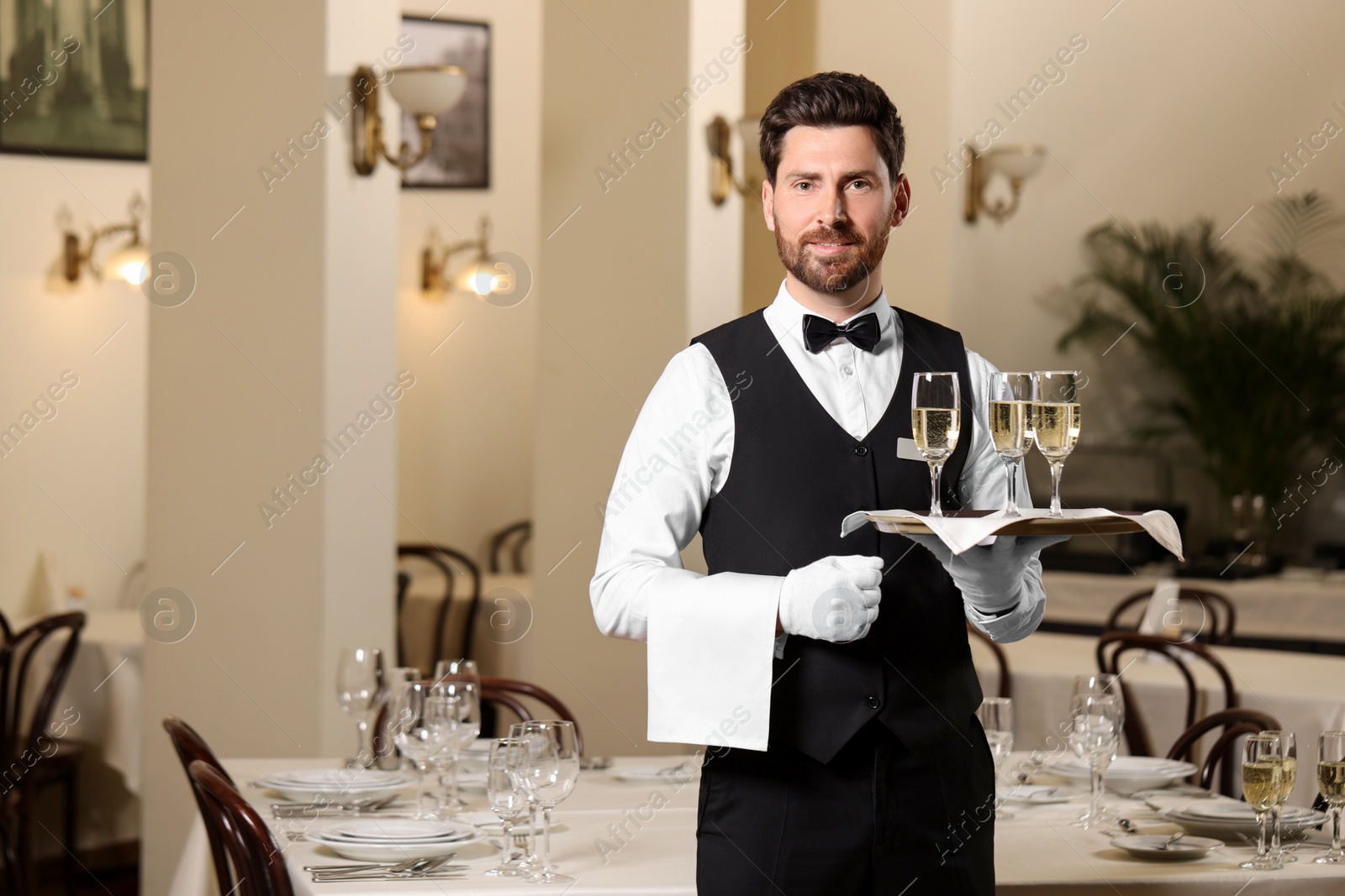 Photo of Butler holding tray with glasses of sparkling wine in restaurant. Space for text