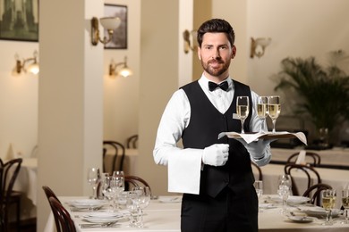 Photo of Butler holding tray with glasses of sparkling wine in restaurant. Space for text