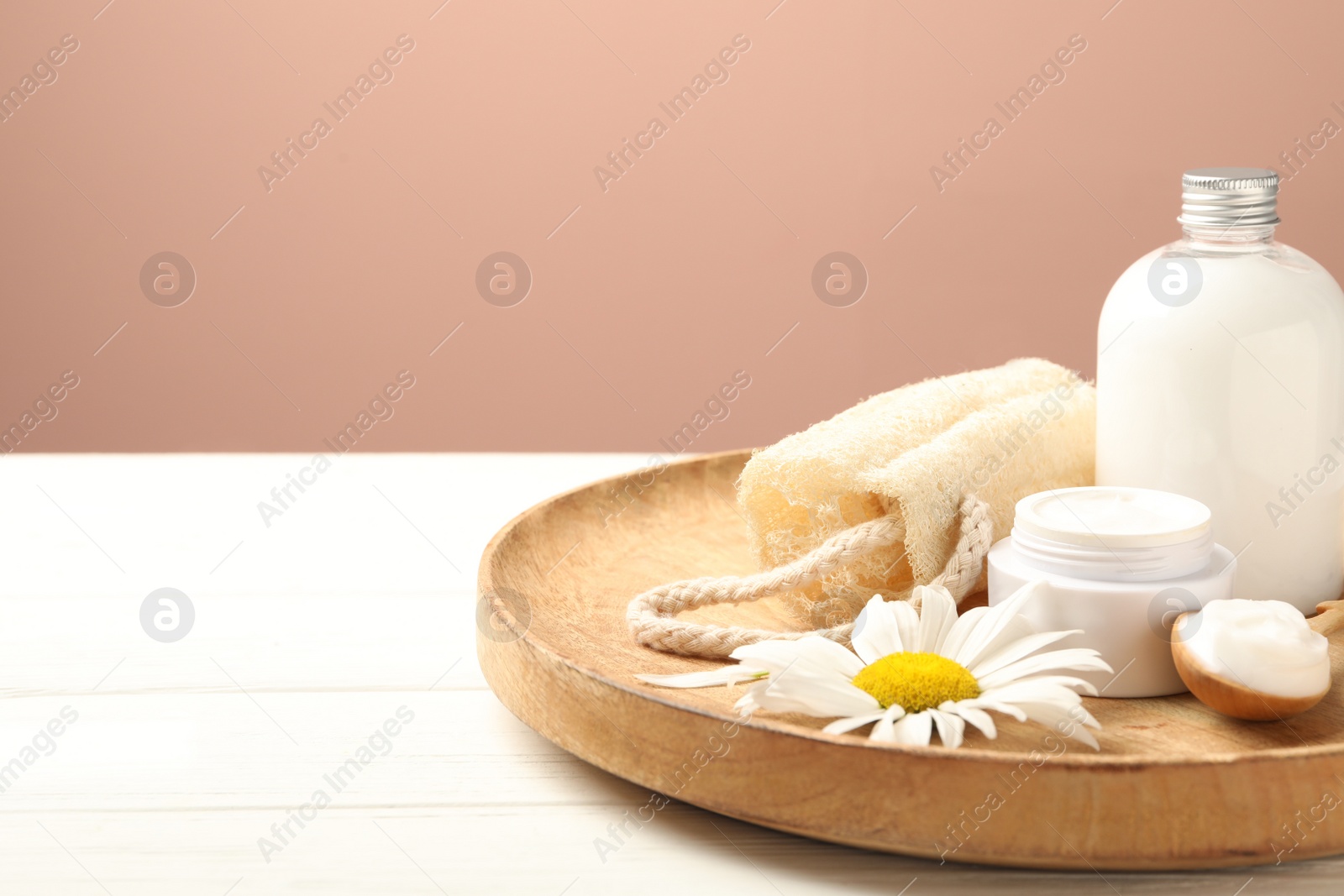 Photo of Cosmetic products, chamomile and loofah on white wooden table against pink background