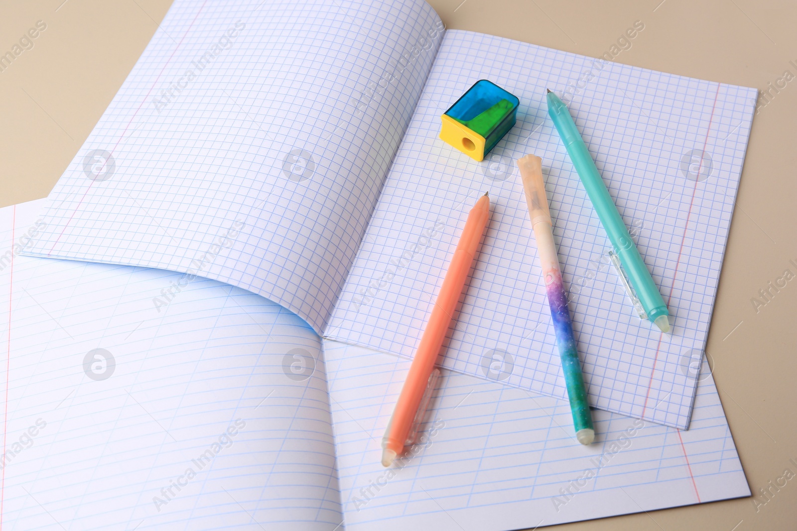Photo of Copybooks with erasable pens and pencil sharpener on beige background
