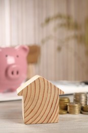 House model, stacked coins, piggy bank and notebook on wooden table, selective focus