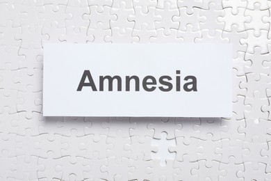 Photo of Card with word Amnesia on white puzzle pieces, top view