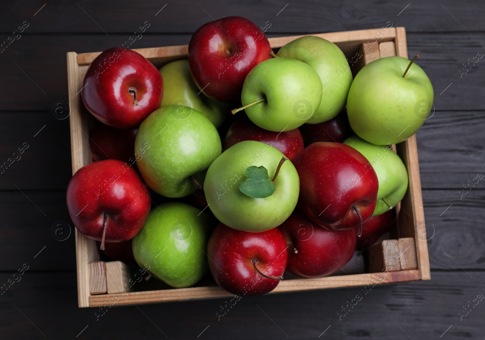 Photo of Fresh ripe red and green apples in wooden crate on black table, top view