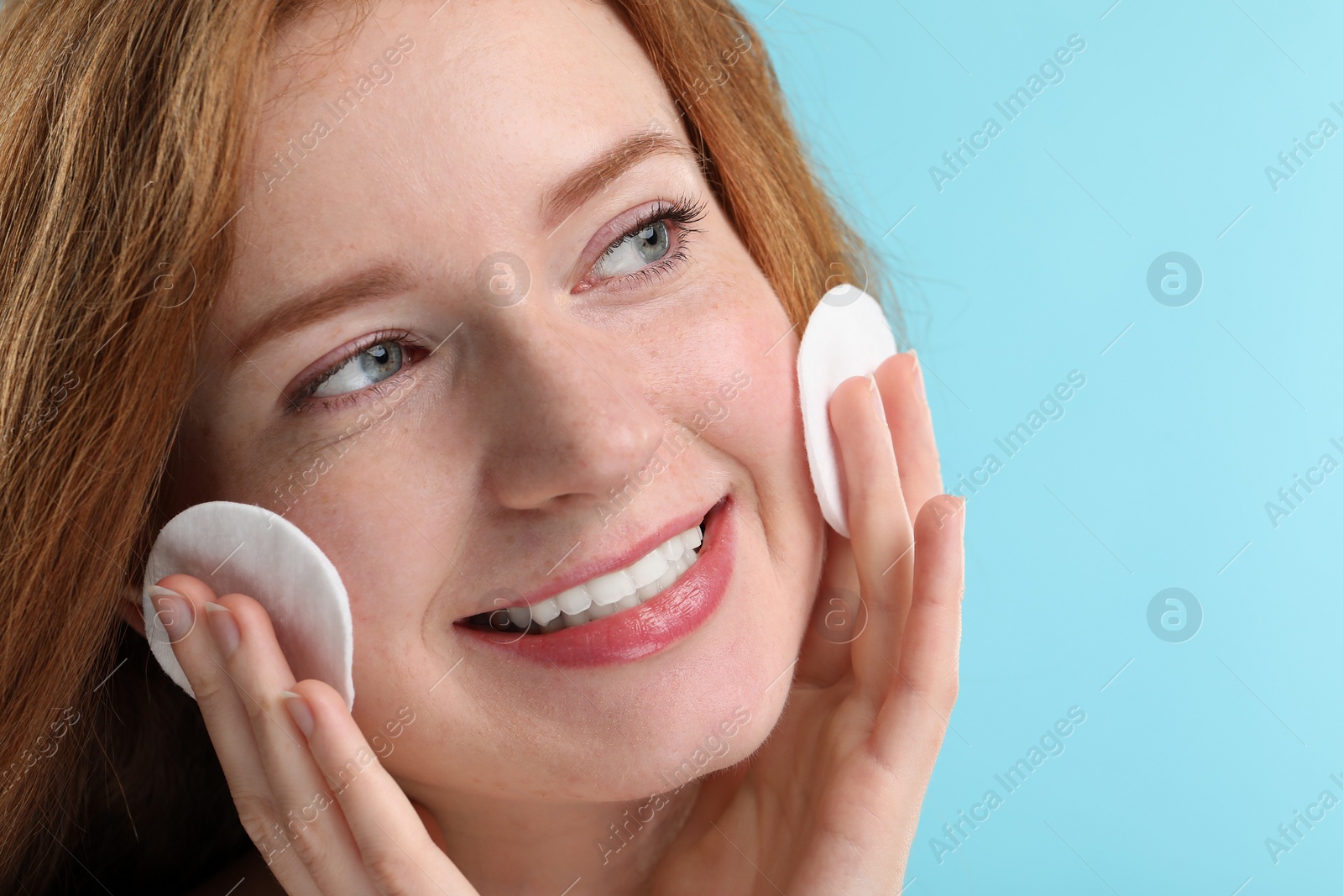 Photo of Smiling woman with freckles wiping face on light blue background, closeup. Space for text