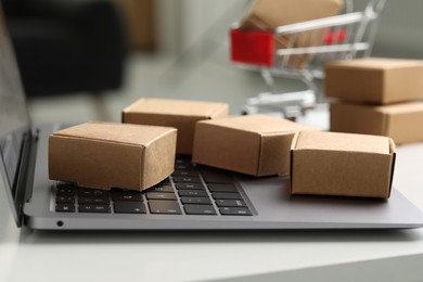 Photo of Online store. Small parcels and laptop on white table, closeup