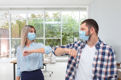 Photo of Office employees in masks greeting each other by bumping elbows at workplace