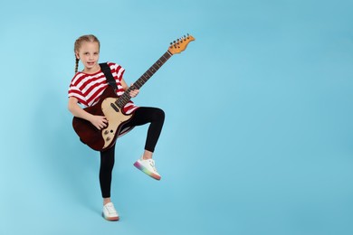Cute girl with electric guitar on light blue background. Space for text